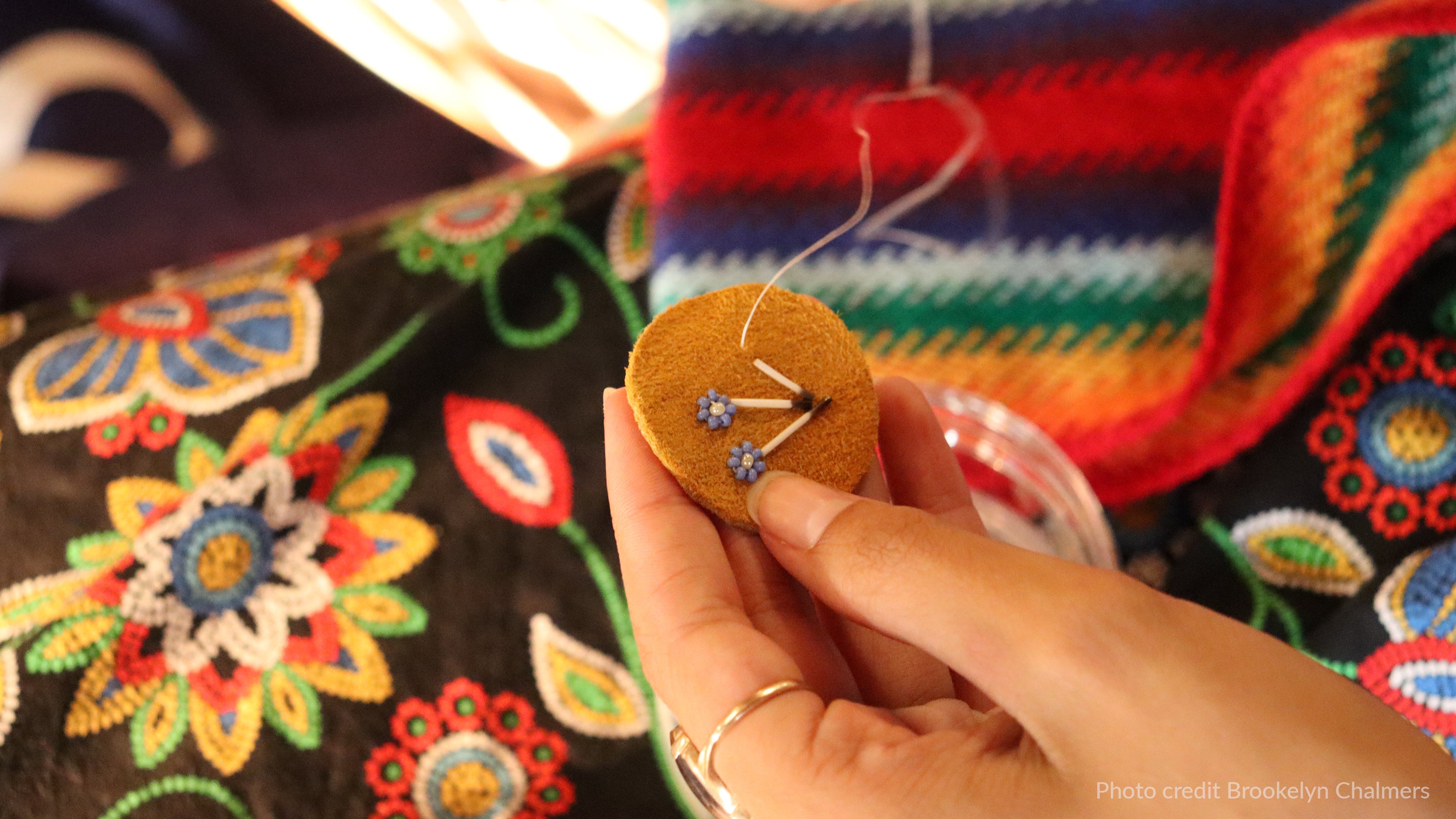 Hand holding a small embroidered piece with colorful fabric in the background