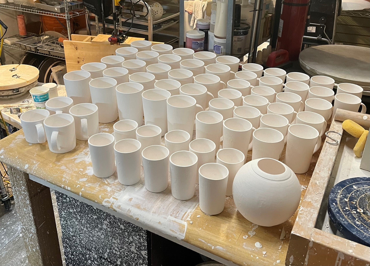 Collection of white ceramic mugs and vases on a workbench in a pottery studio.