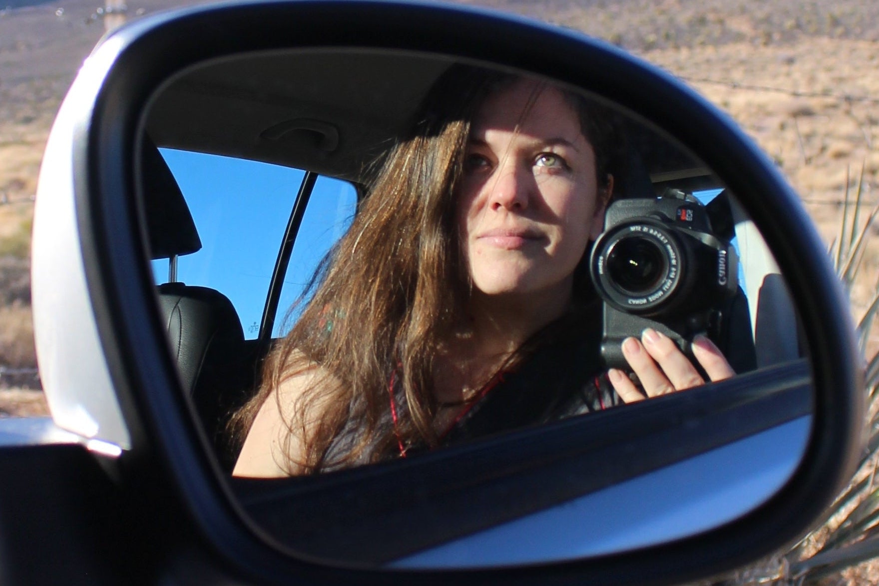Woman holding a camera in front of a car mirror reflection